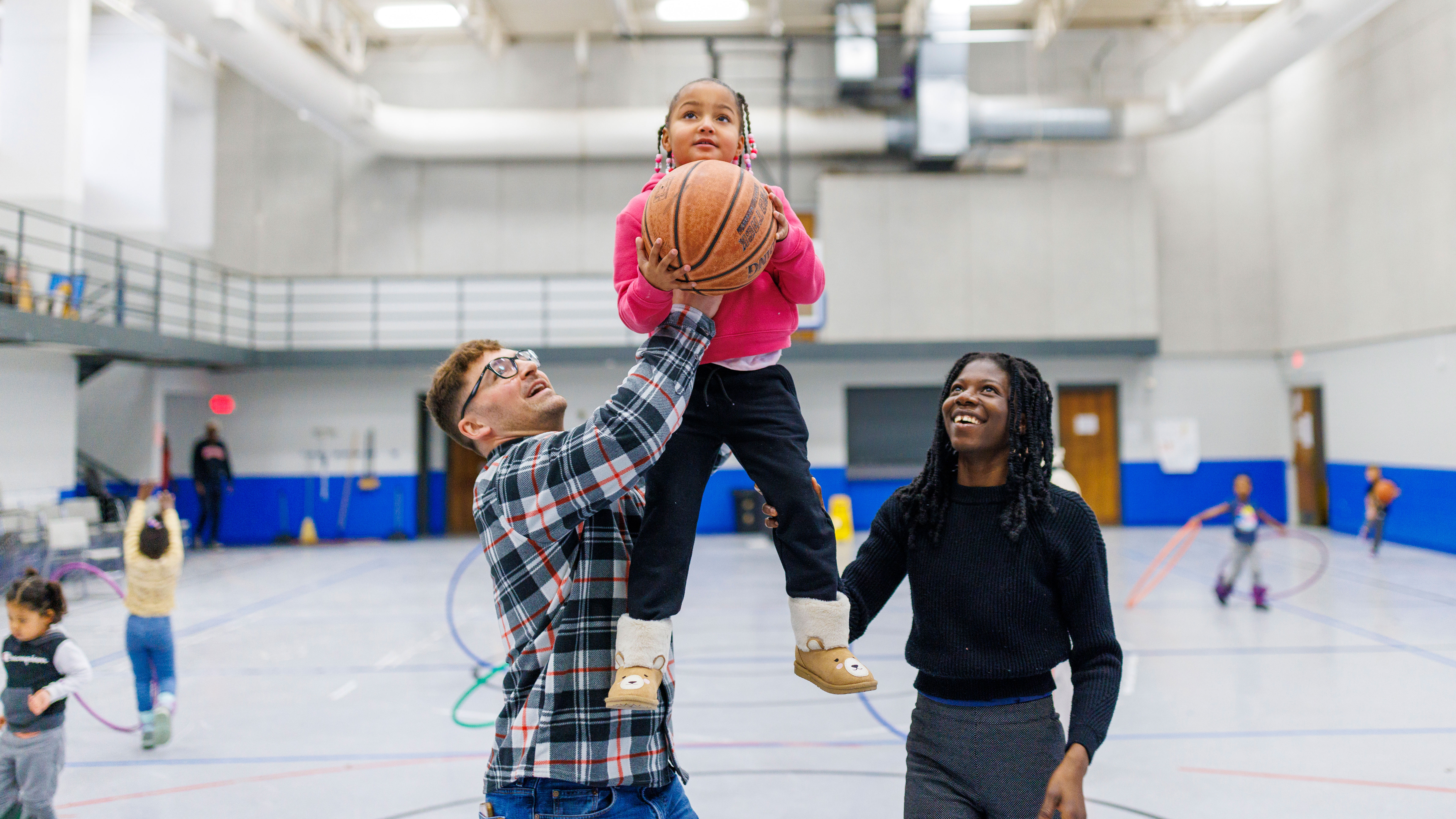 Ben Bentzinger, a senior in criminal justice, and Francisca Lawson Tettevie a graduate student in human sciences, help Journey shoot a basket at the Malone Center.