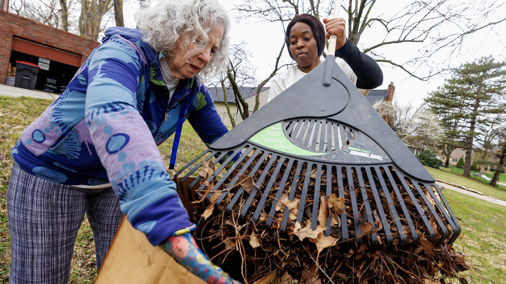 A graduate student and a homeowner work together to bag leaves outside a house during a campus service day.