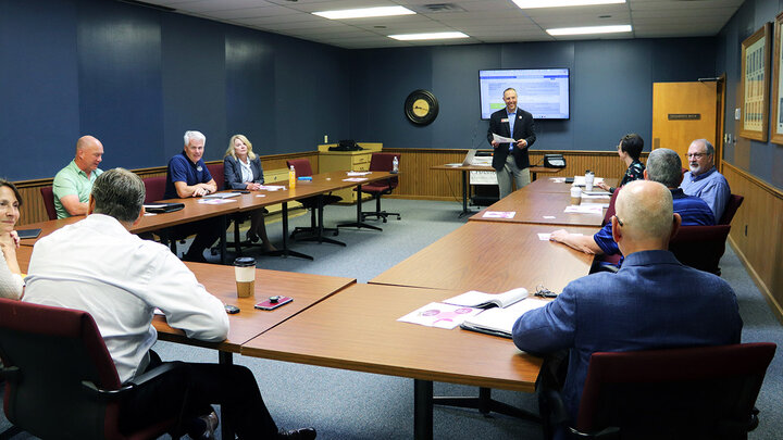 Shawn Kaskie stands in front of tables forming a U shape and nine members, seated, of Grand Island’s eCommunities steering committee.