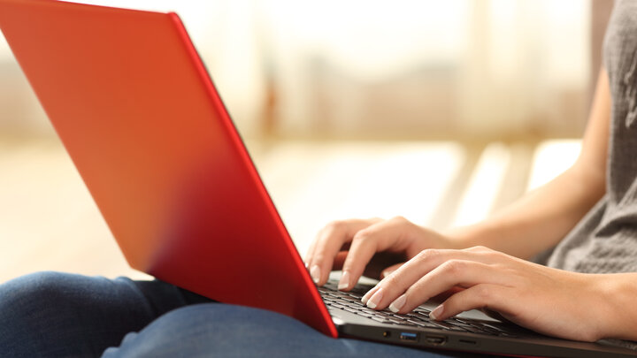 A young woman types on a laptop with a red case.