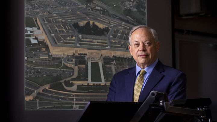 Jack Beard in a dark room, with a photo of the Pentagon in the background
