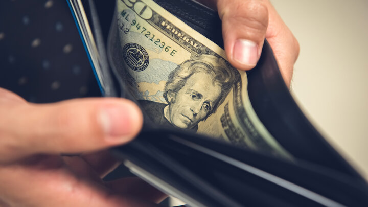 A close-up of hands opening a wallet with a $20 bill inside.