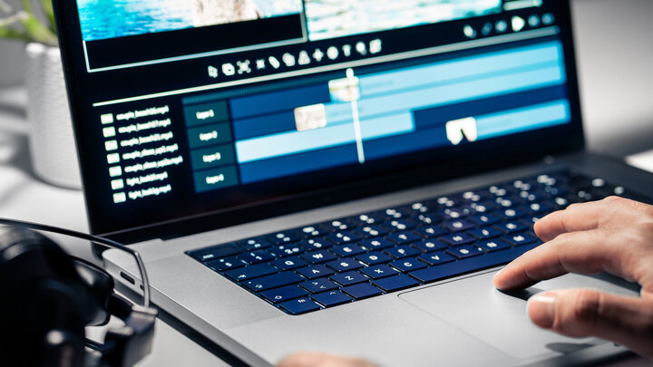 A close-up of a person's hands editing a video on a laptop.