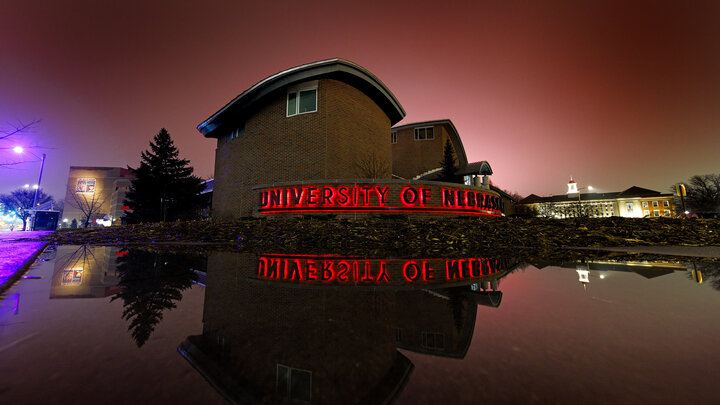 Dusk illuminates the Campus Visitors Center following rains, which reflect the welcome sign.