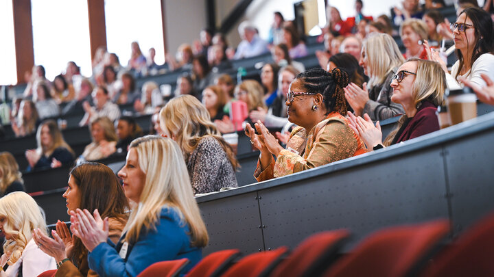 Conference participants sit in chairs listening to a presentation during Women Lead.