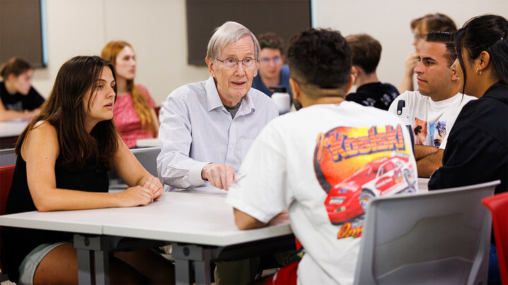 Jim Lewis sits at a table while talking with students
