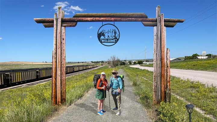 Simulated photo of the trail gateway in Chadron, Nebraska. Shows two people standing under a "welcome" gateway arch made of wood.