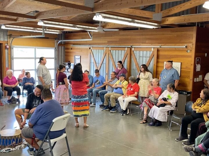 Two dozen or so people sit in a circle playing a traditional Indigenous guessing game called a hand game at the Spring Creek Prairie Audubon Center.
