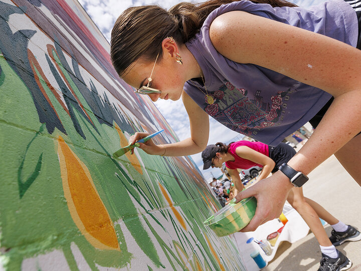 Lea Bushey, a senior in graphic design, paints stems of grass on the mural. ARTS 398 - Special Topics in Studio Art III taught by Sandra Williams. The class painted a mural at the Premier Buick, Chevrolet, and GMC dealership in Beatrice.
